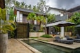 A pool in front of a house surrounded by greenery
