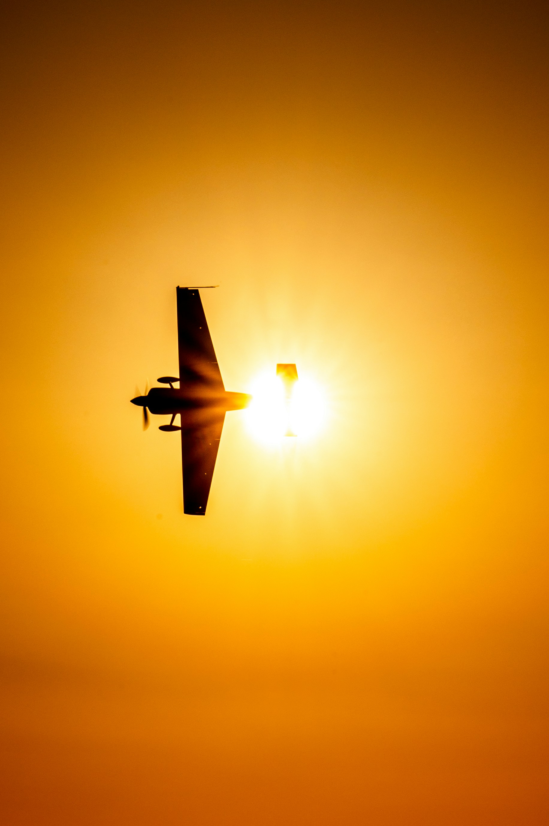 A plane flying in the sky with the sun in the background