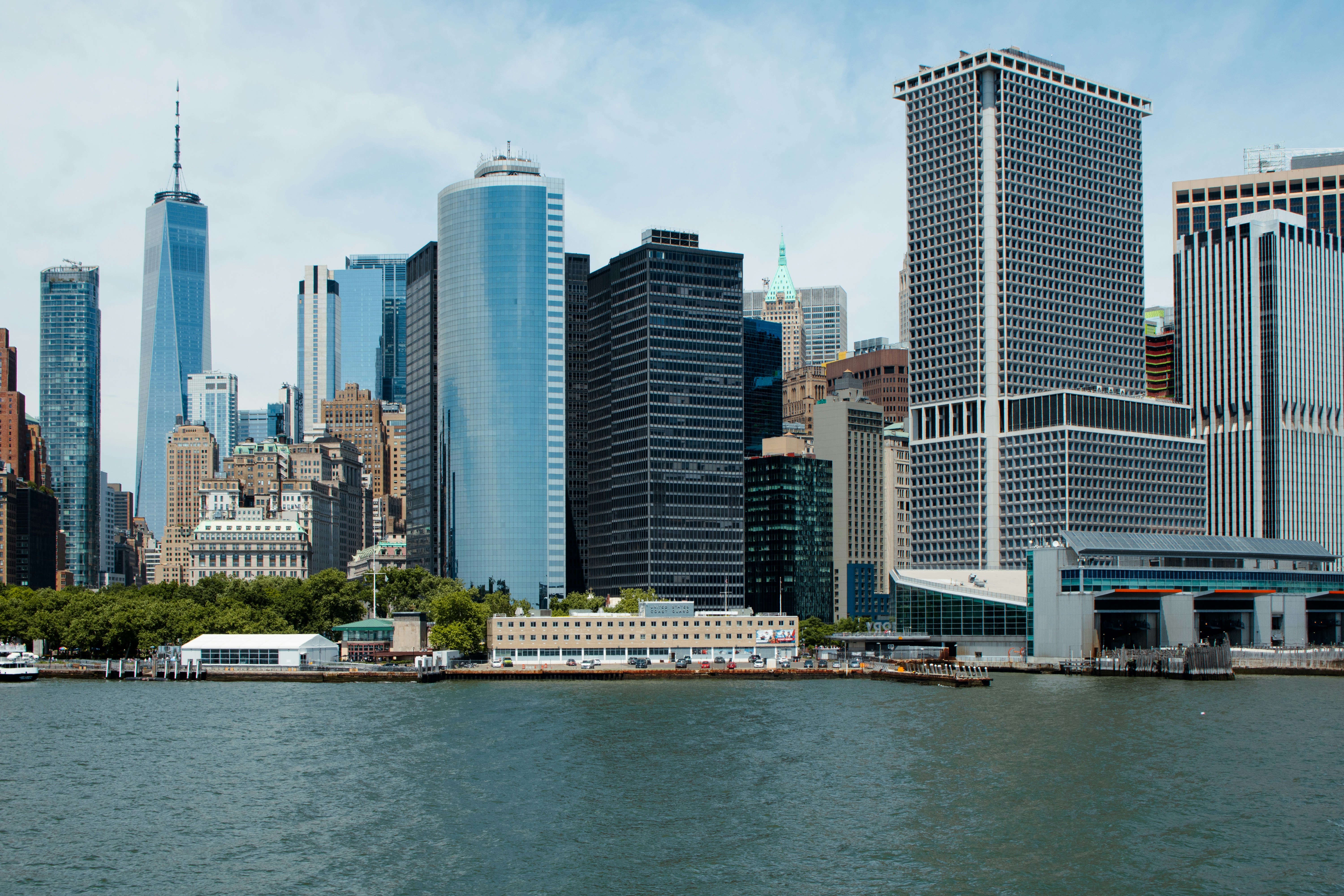 A large body of water with a city in the background, The tip of the lower Manhattan New York City skyline as seen from the Staten Island Ferry in New York City Harbor. The skyline features One World Trade Center, One State Street Plaza, One New York Plaza, and the Staten Island Ferry Terminal.
