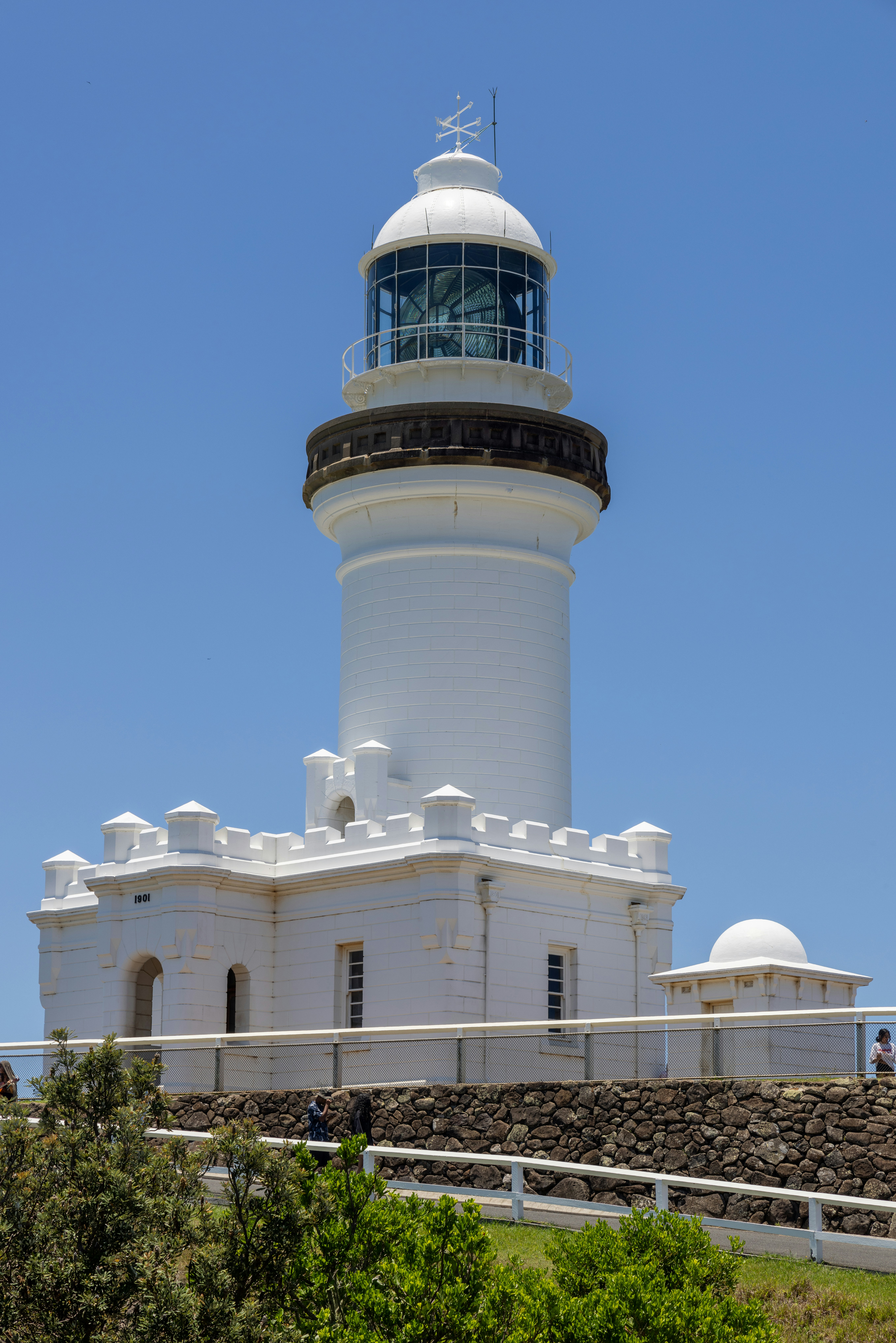 A white lighthouse on a hill with a blue sky in the background