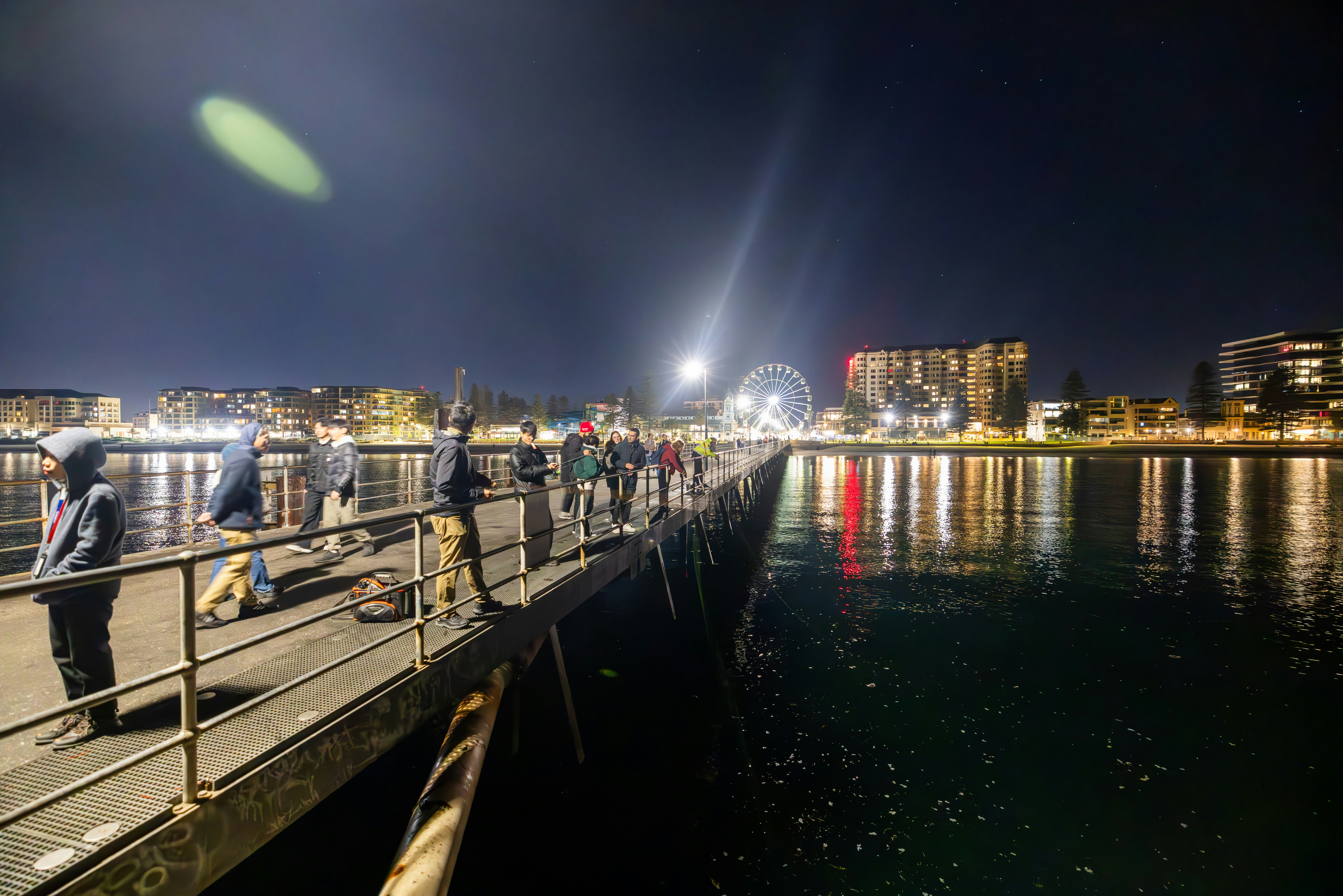 A group of people standing on a pier next to a body of water