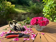 A wooden table topped with pink flowers and gardening utensils