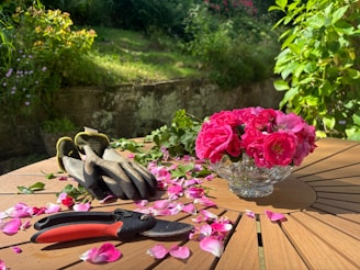 A wooden table topped with pink flowers and gardening utensils