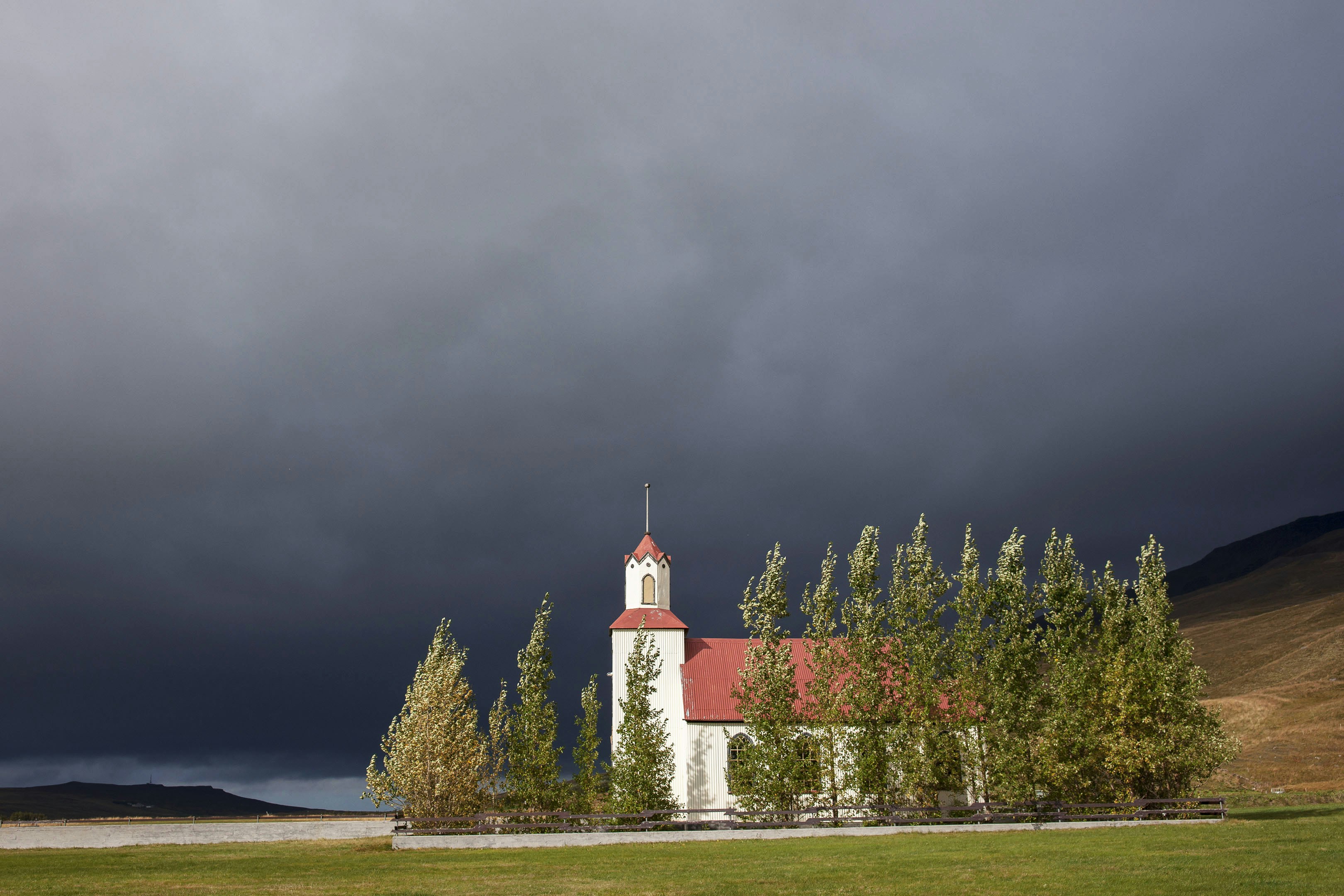 A white church with a red roof under a cloudy sky