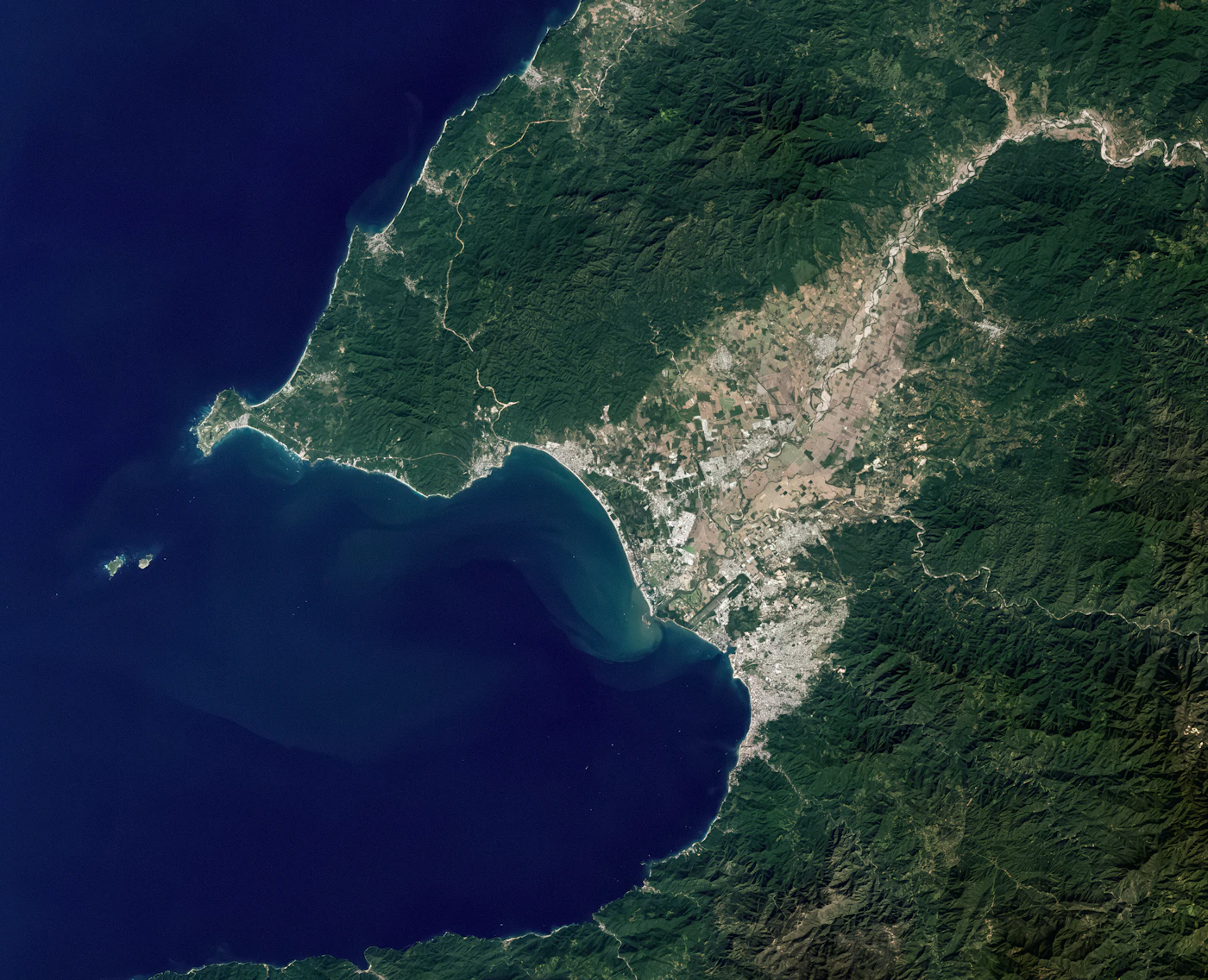 A satellite view of a coastal city beside a bay, with the model's change outlines drawn over it.