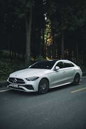 A white car driving down a street next to a forest