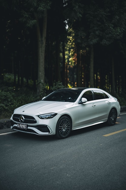 A white car driving down a street next to a forest