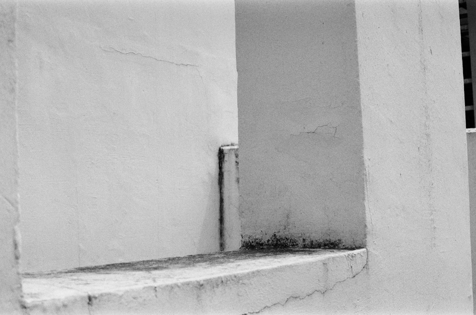 White building with a closed, concrete-framed window featuring a vertical line on its right side