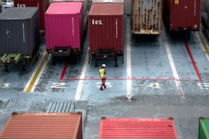 A man standing in a parking lot next to lots of shipping containers
