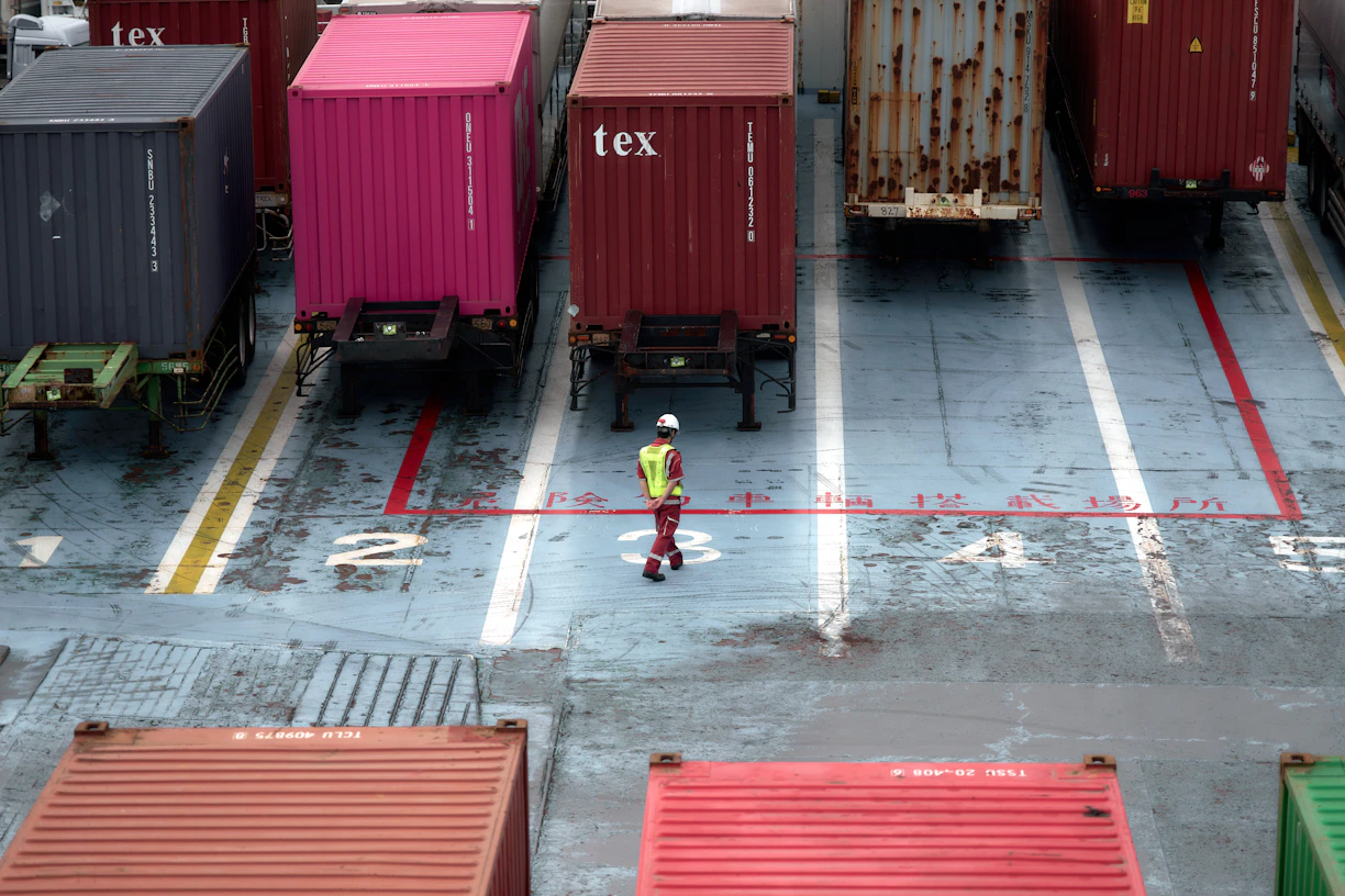 A man standing in a parking lot next to lots of shipping containers