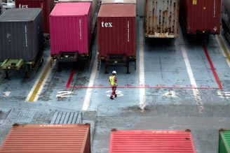 A man standing in a parking lot next to lots of shipping containers