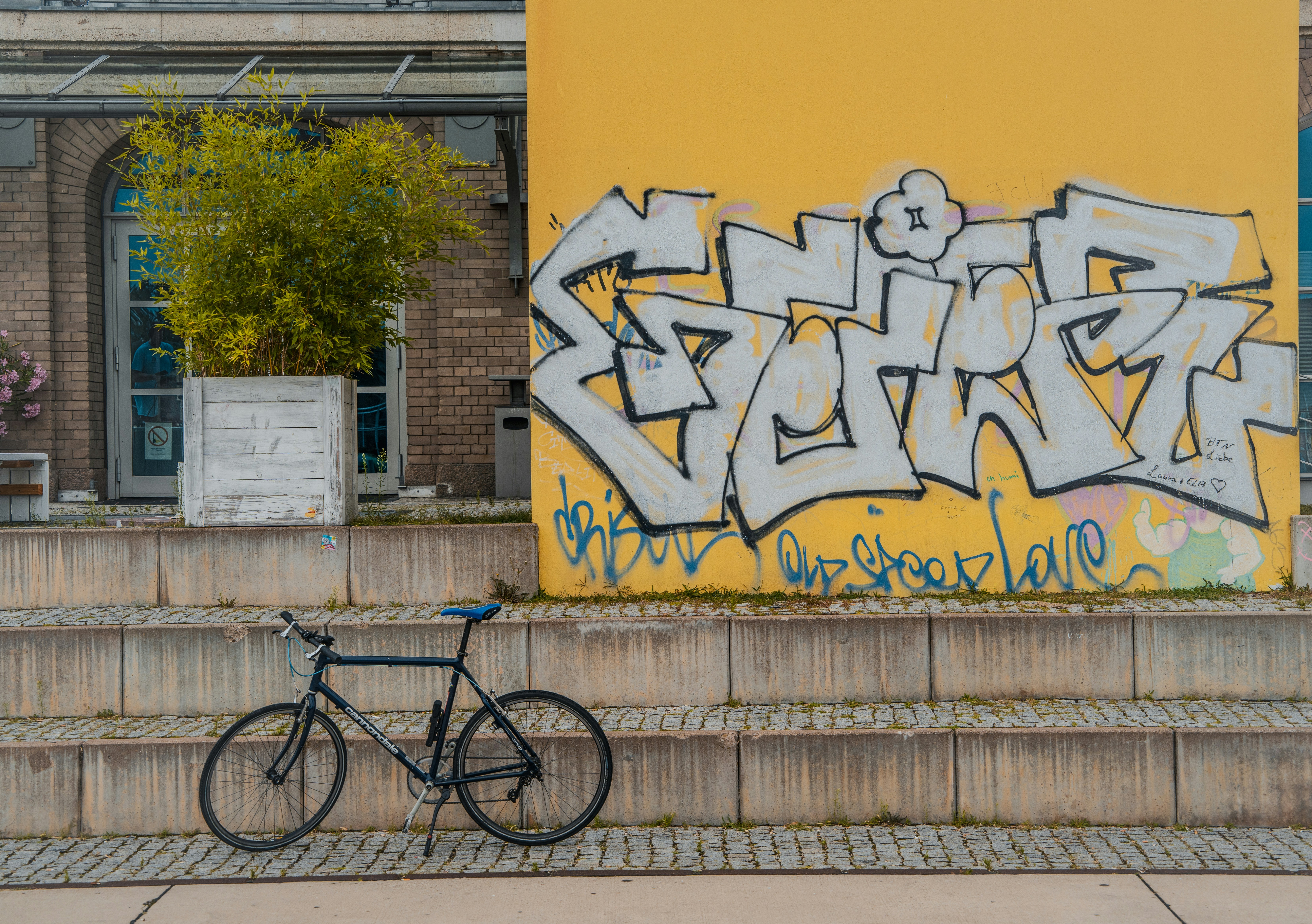 A bike parked in front of a yellow wall with graffiti