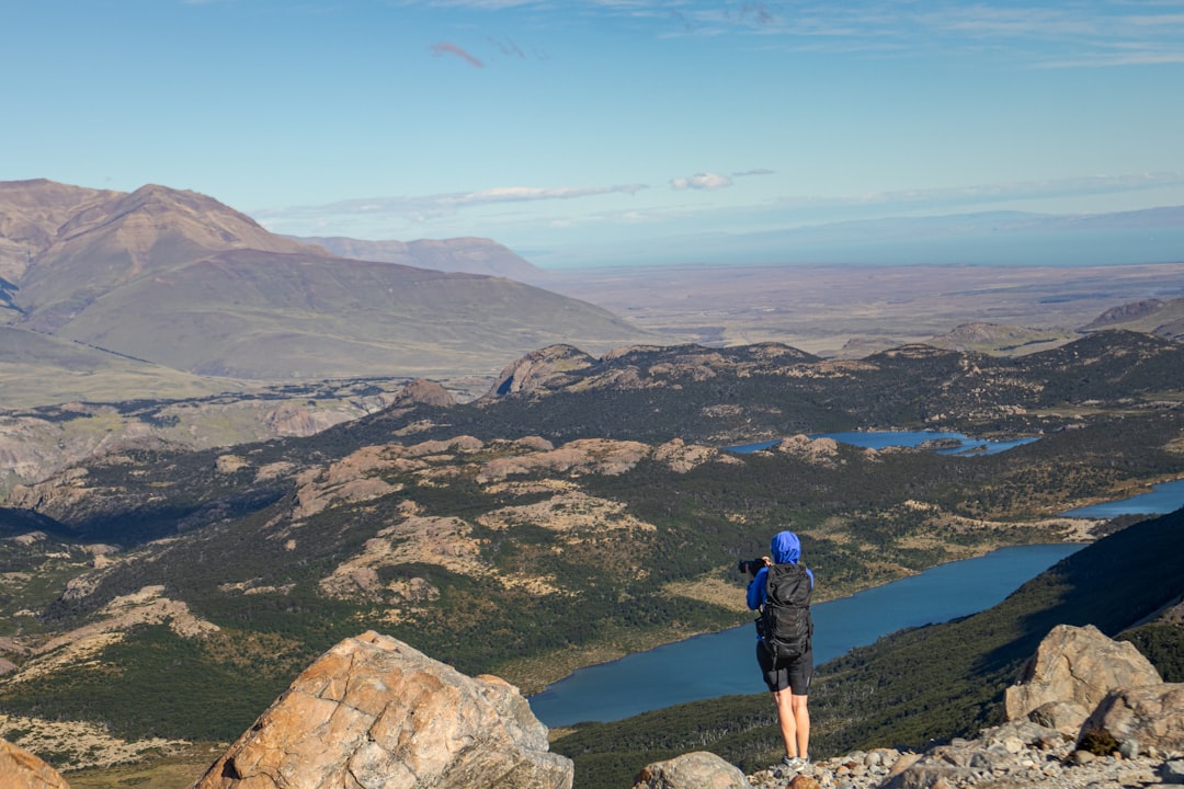 A person standing on top of a mountain overlooking a valley, Woman taking pictures from Laguna de Los Tres