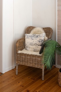 A wicker chair with a pillow on top of it and faux fur throw, next to a potted green plant