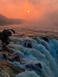 The sun is setting over the water and rocks