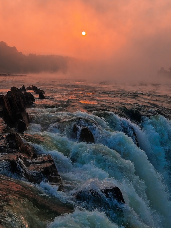 The sun is setting over the water and rocks
