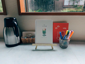 A desk with a coffee pot, notepad, pencils and a coffee pot