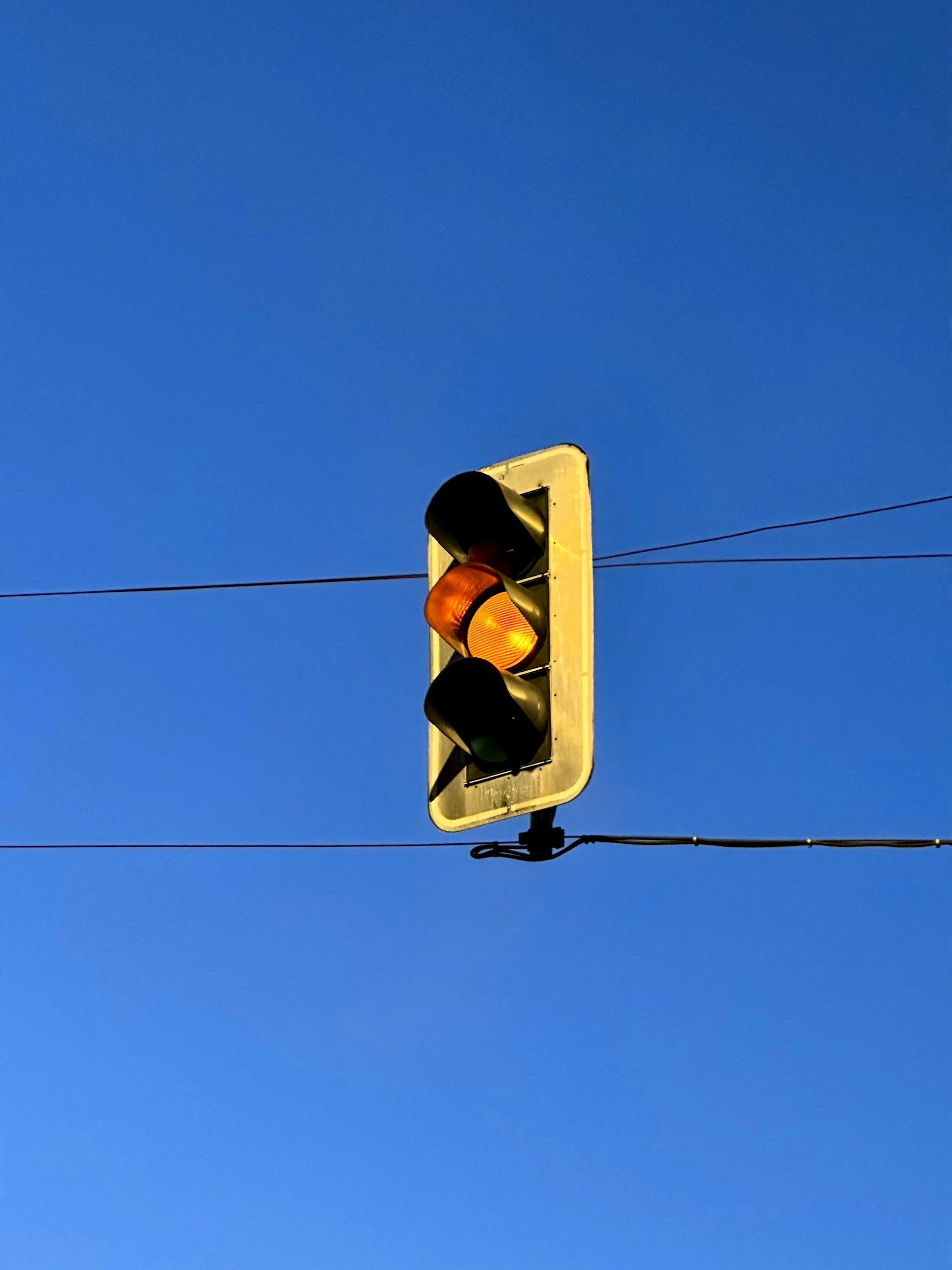 A traffic light hanging from a wire against a blue sky