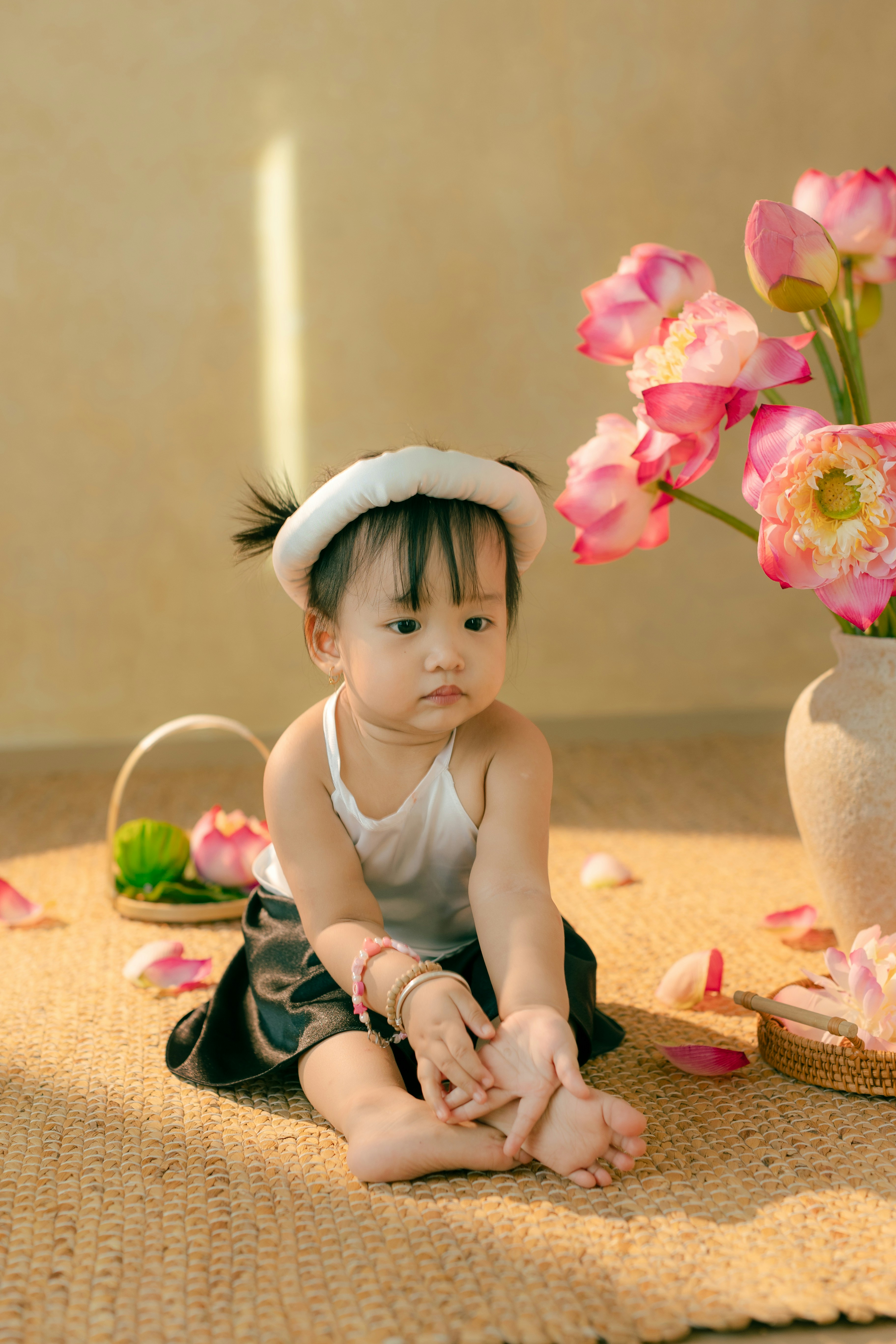 A little girl sitting on the floor next to a vase of flowers
