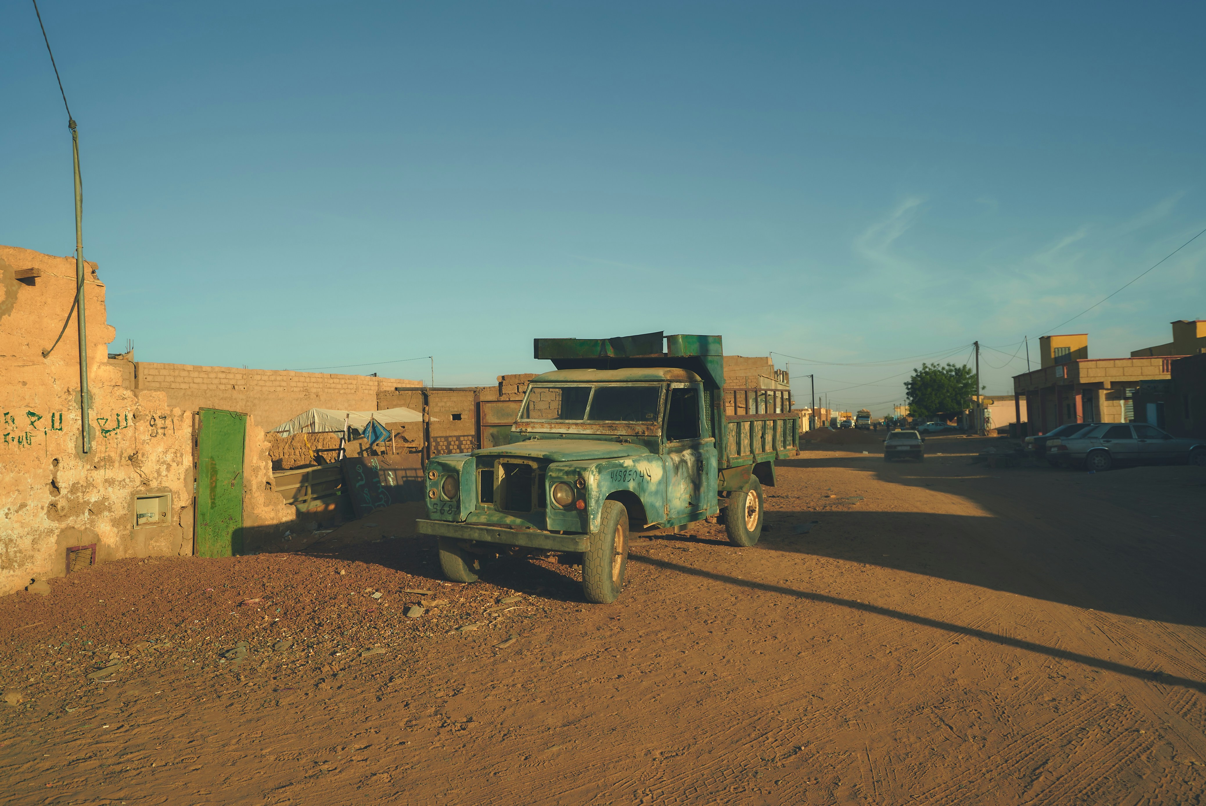 An old green truck parked on the side of a dirt road