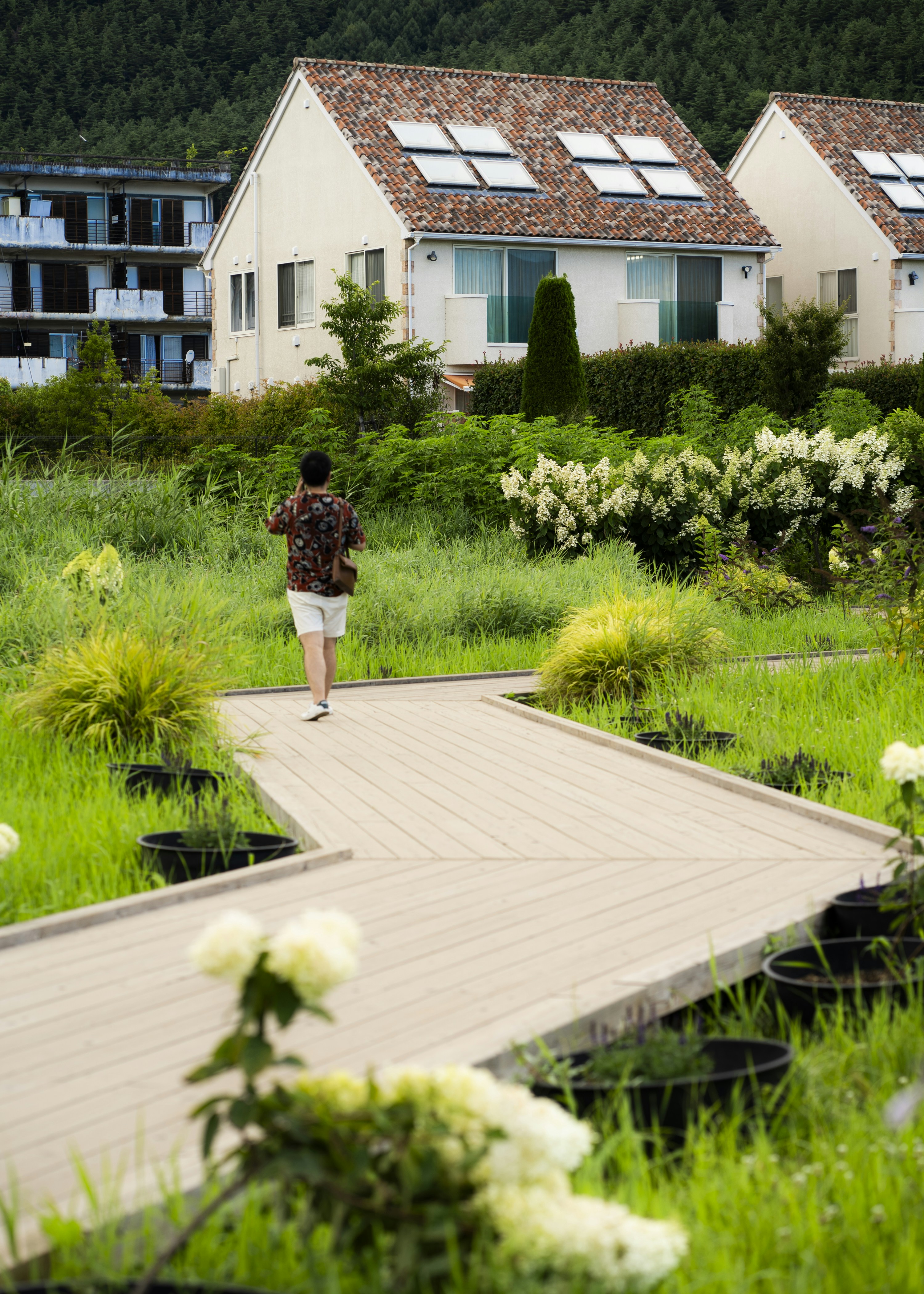 A man walking across a wooden walkway next to a lush green field