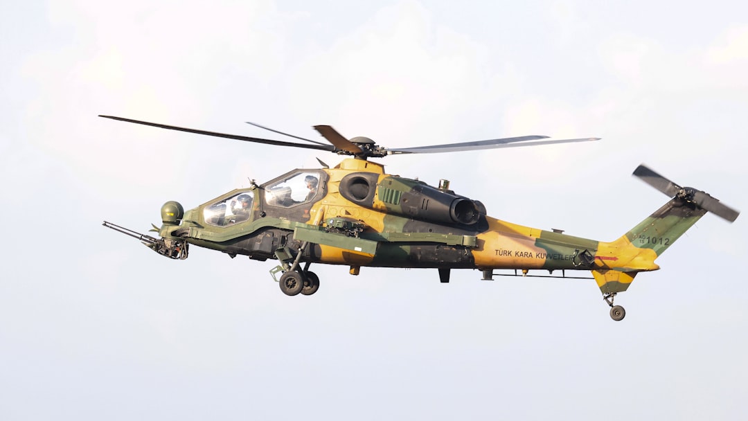 A yellow and green helicopter flying in the sky, The T129 ATAK, a powerful military helicopter, is in mid-flight, showcasing its robust and tactical design.
