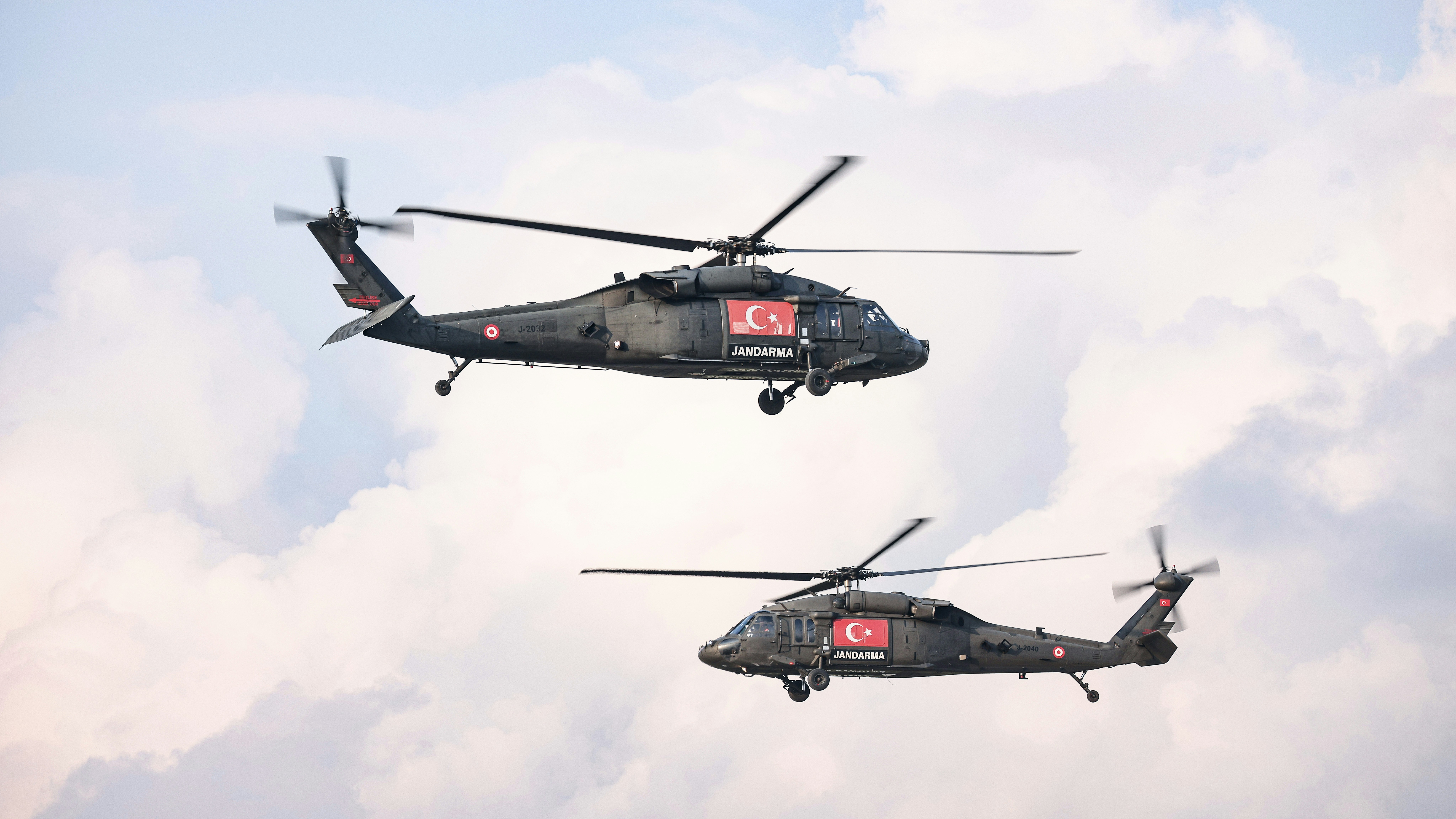 Two military helicopters flying through a cloudy sky