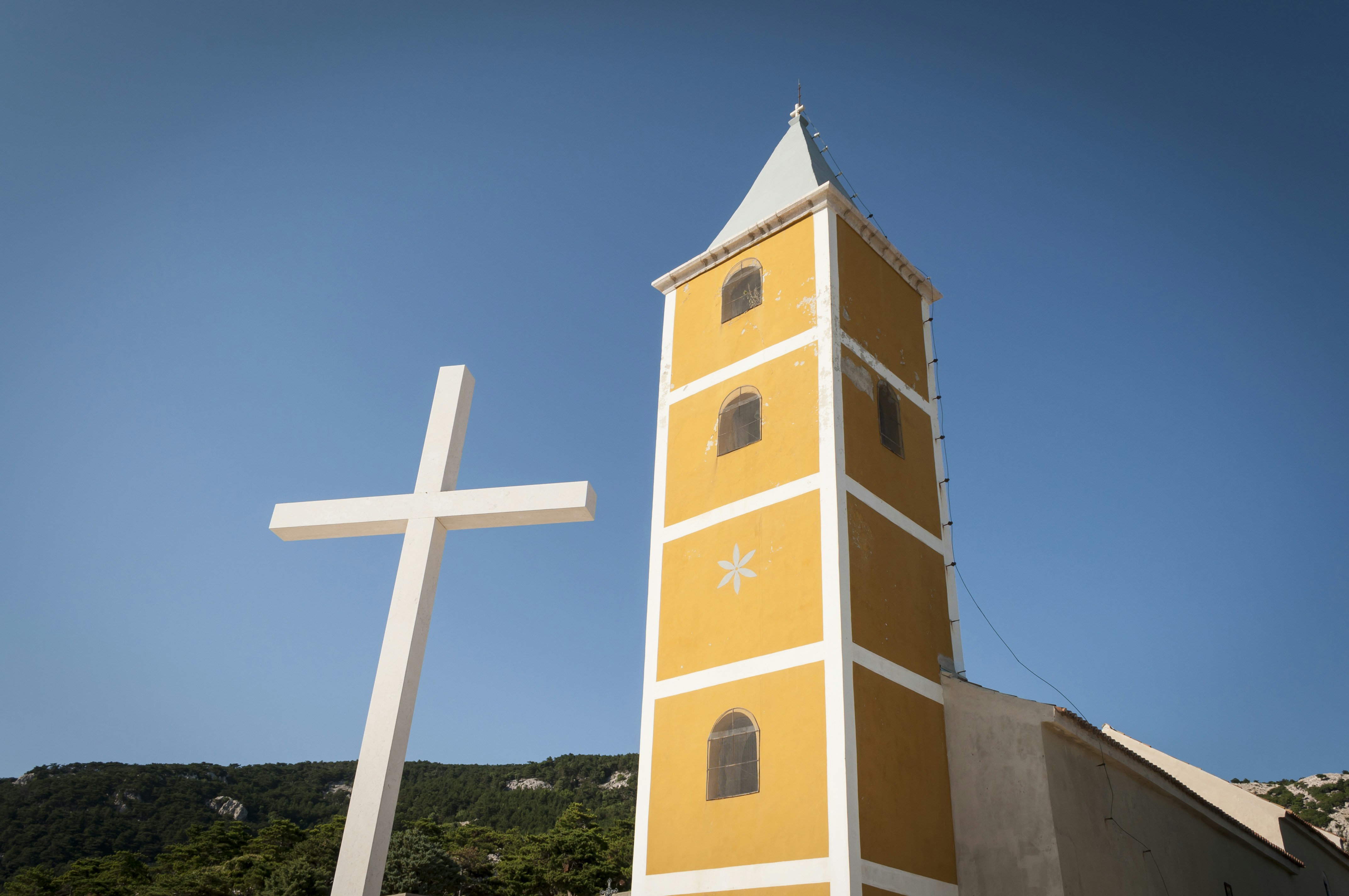 A yellow and white church with a cross in front of it