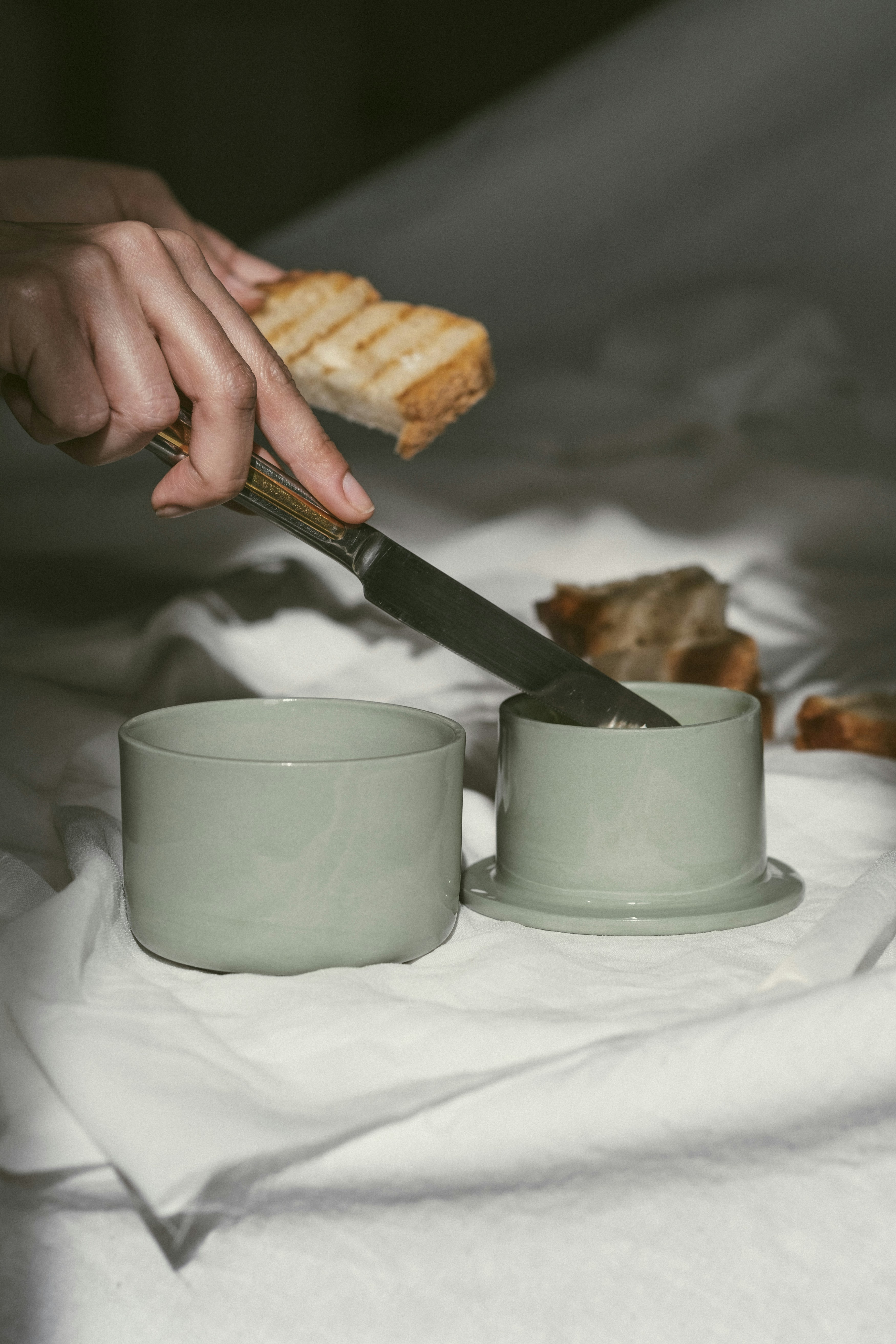 A person holding a knife and cutting a piece of bread