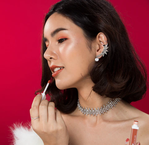 A woman in a white dress is putting lipstick on her lips