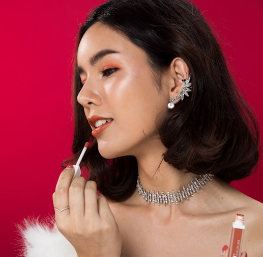 A woman in a white dress is putting lipstick on her lips