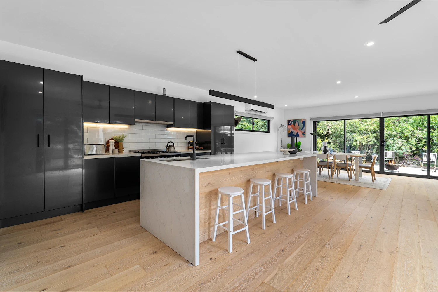 A dark-fronted kitchen running into a dining space under a long window