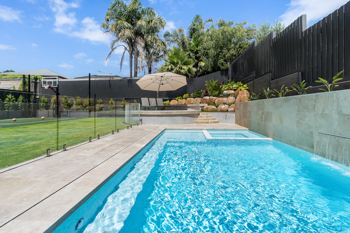 A frameless glass pool fence beside a dark timber privacy fence.
