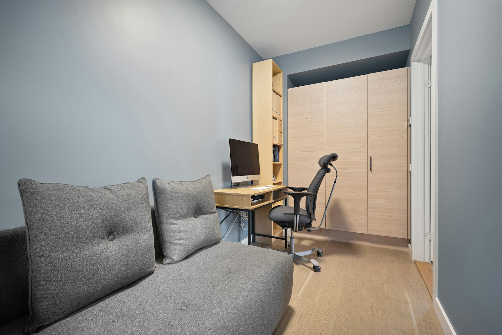 studio apartment with desk, monitor, and grey couch sharing one room