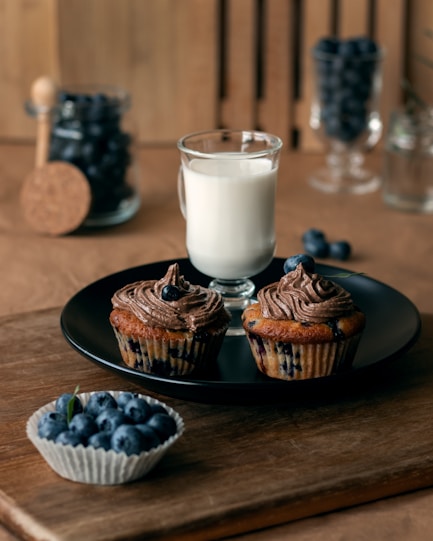 A plate of blueberry muffins next to a glass of milk