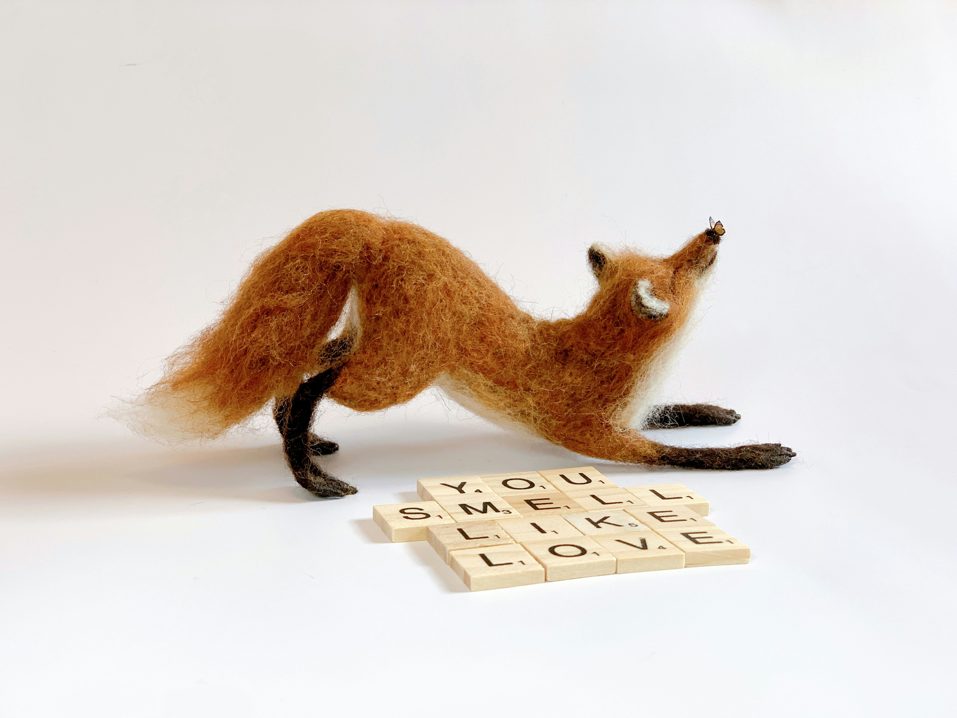 A toy fox laying on its back next to a scrabble