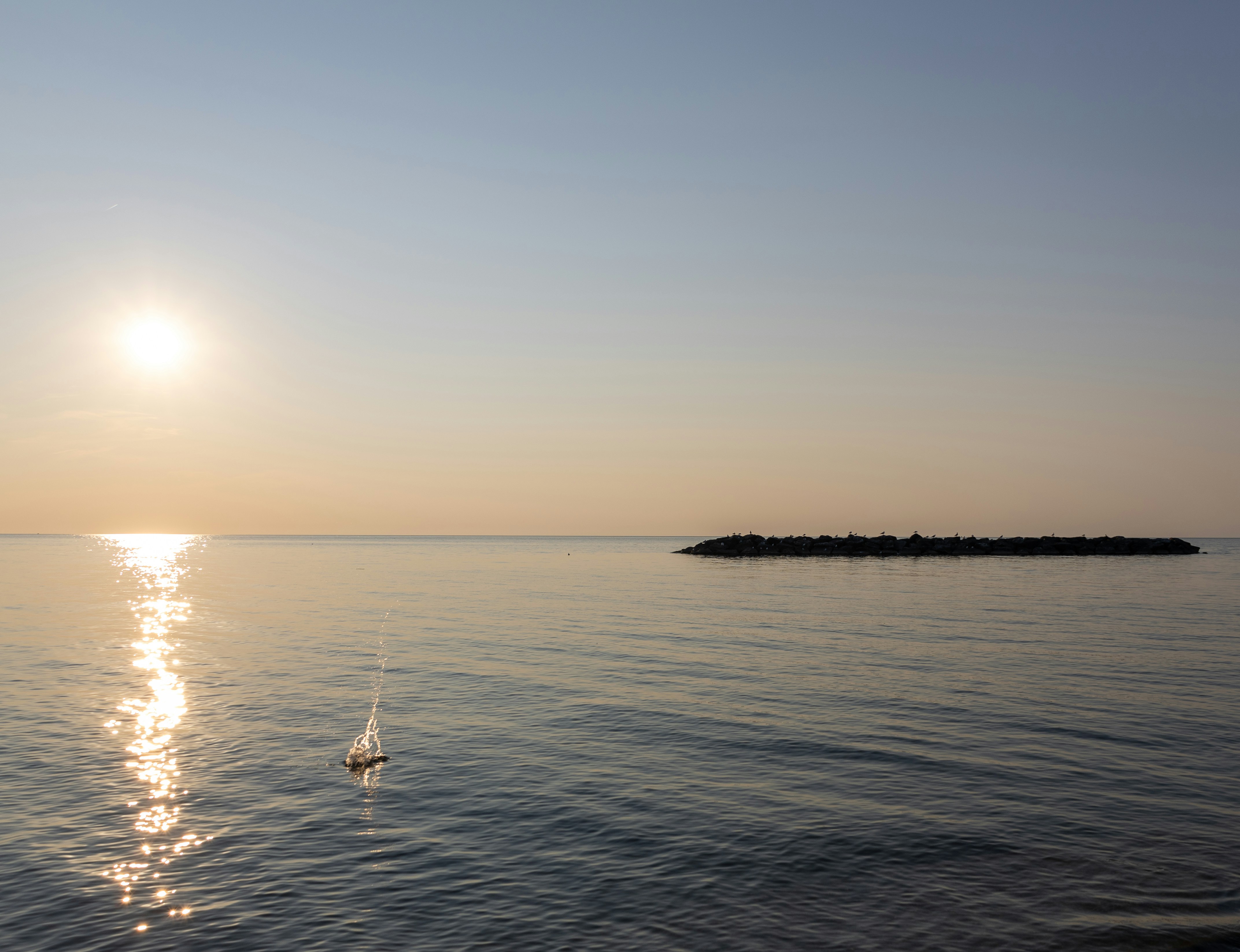 The sun is shining over the water with a small boat in the distance
