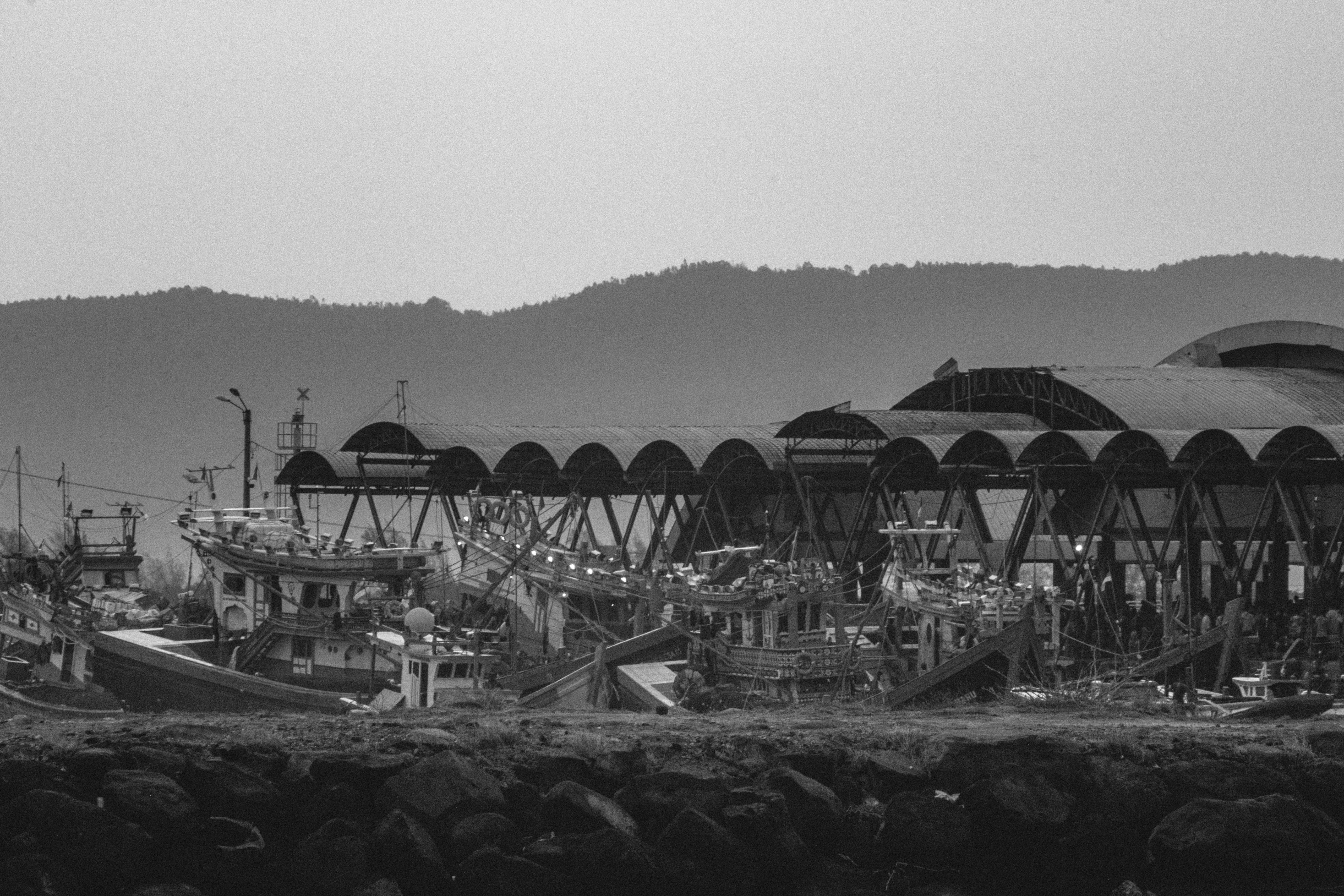 A black and white photo of a pier with boats and umbrellas