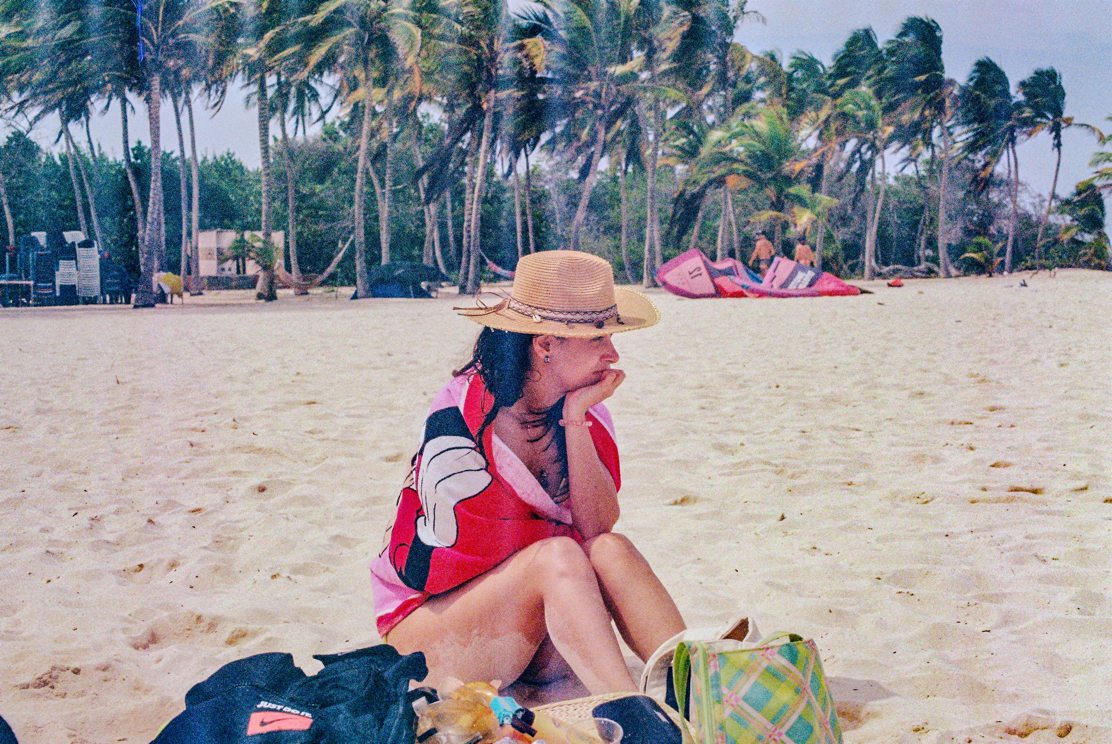 A woman sitting on a beach next to luggage