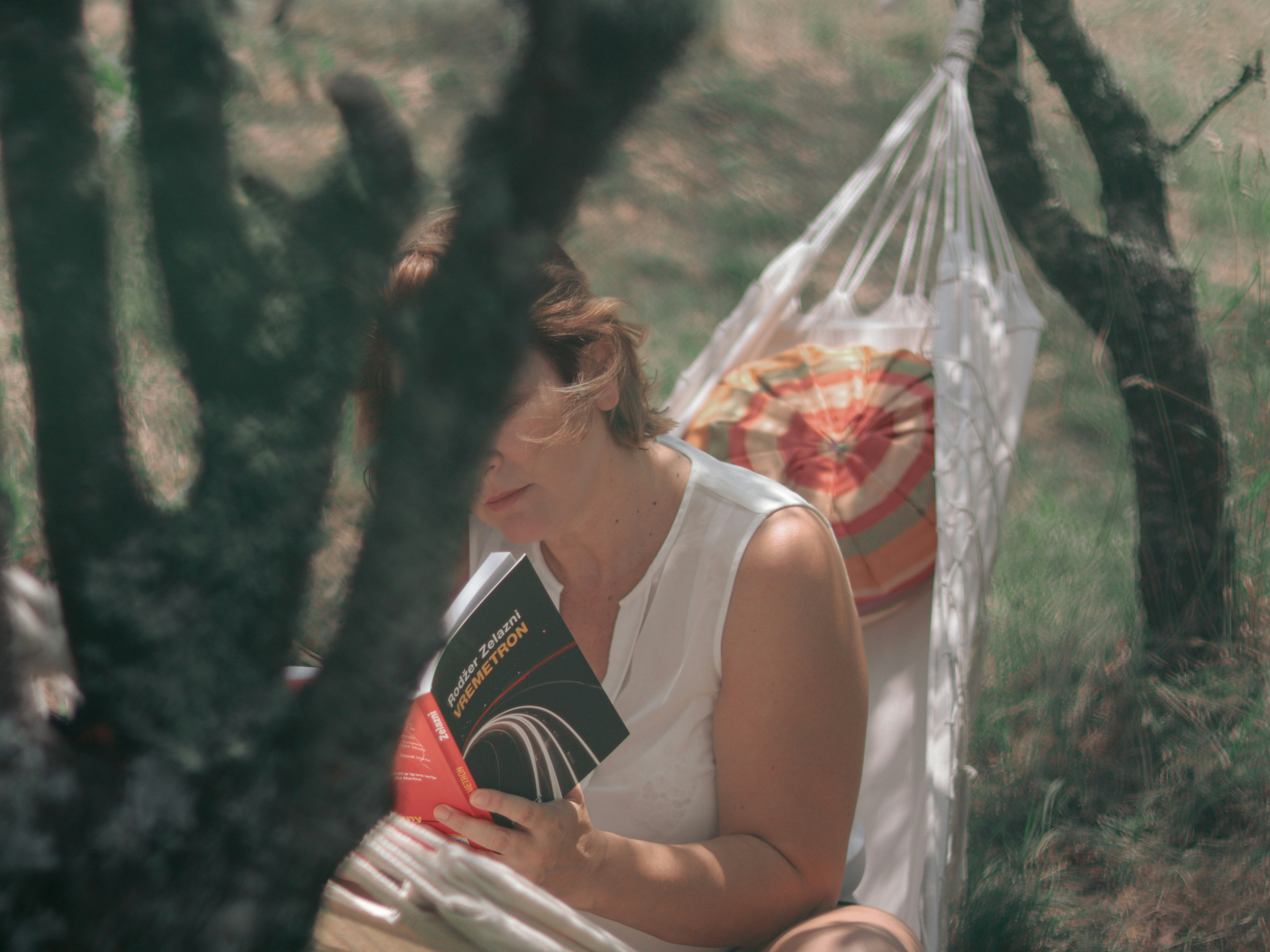 A person smiling while reading a book in a hammock.