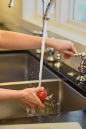 A person washing an apple under a faucet
