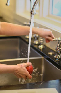 A person washing an apple under a faucet