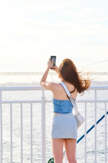 A woman taking a picture of the ocean with her cell phone