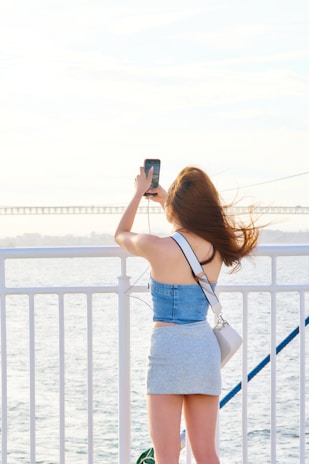 A woman taking a picture of the ocean with her cell phone