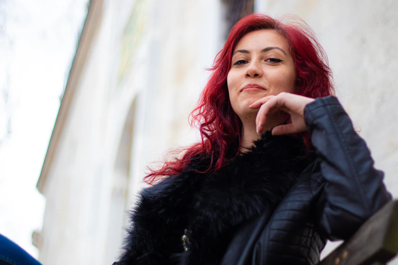 A woman with red hair is leaning against a wall