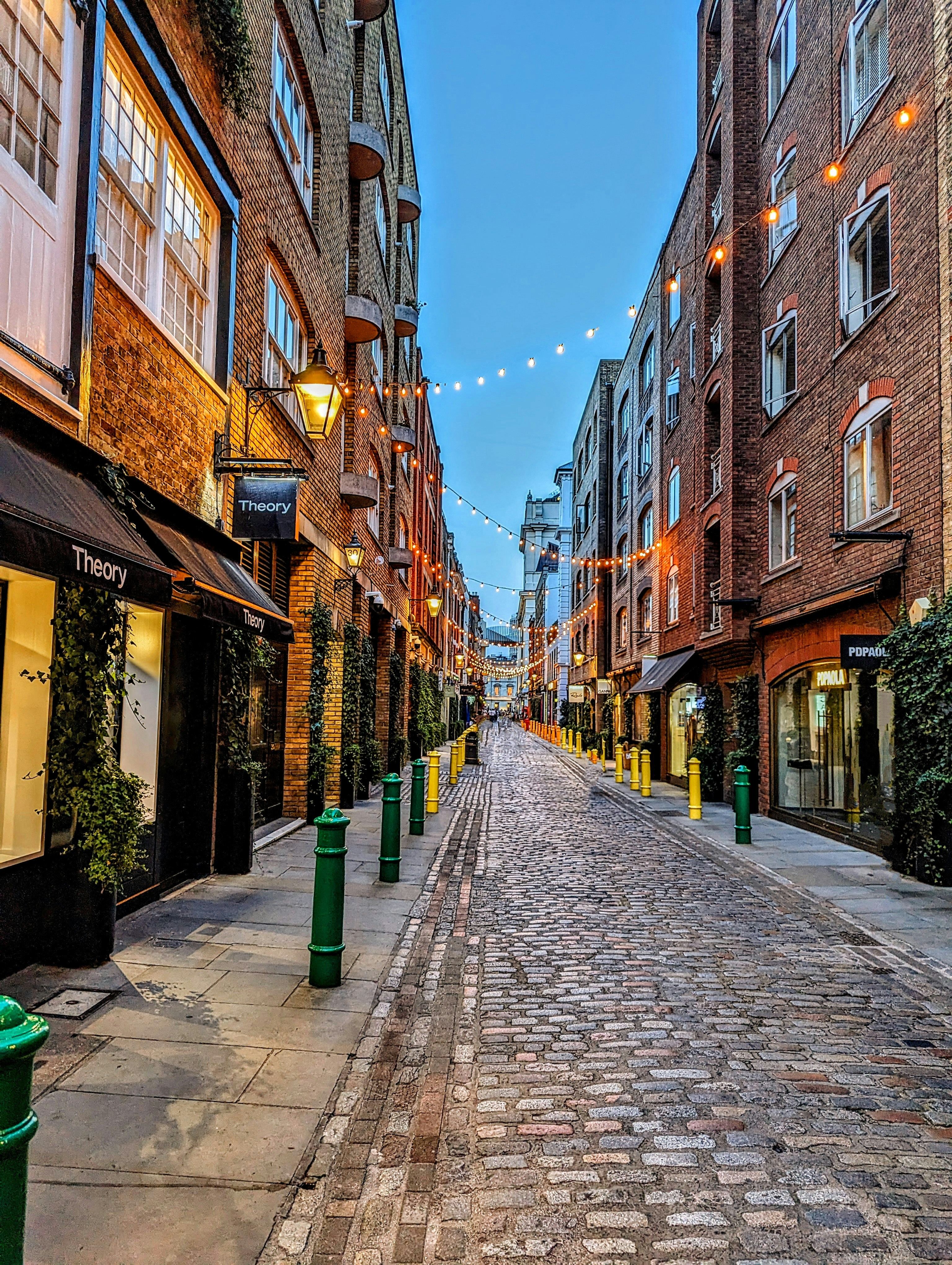 A cobblestone street lined with buildings and green trash cans