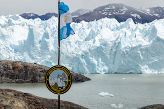 A flag pole in front of a glacier with mountains in the background