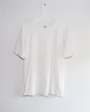 White tee hanging on a white wall — placeholder photo