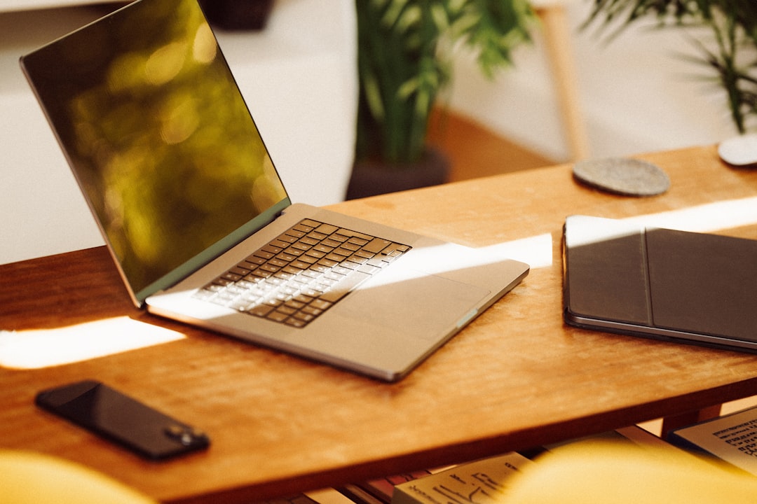 A laptop computer sitting on top of a wooden desk, Living room interior with electronic office devices.