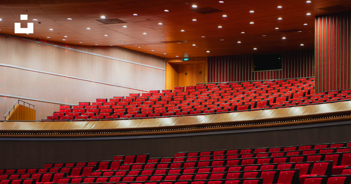A large auditorium filled with red seats and a projector screen photo ...